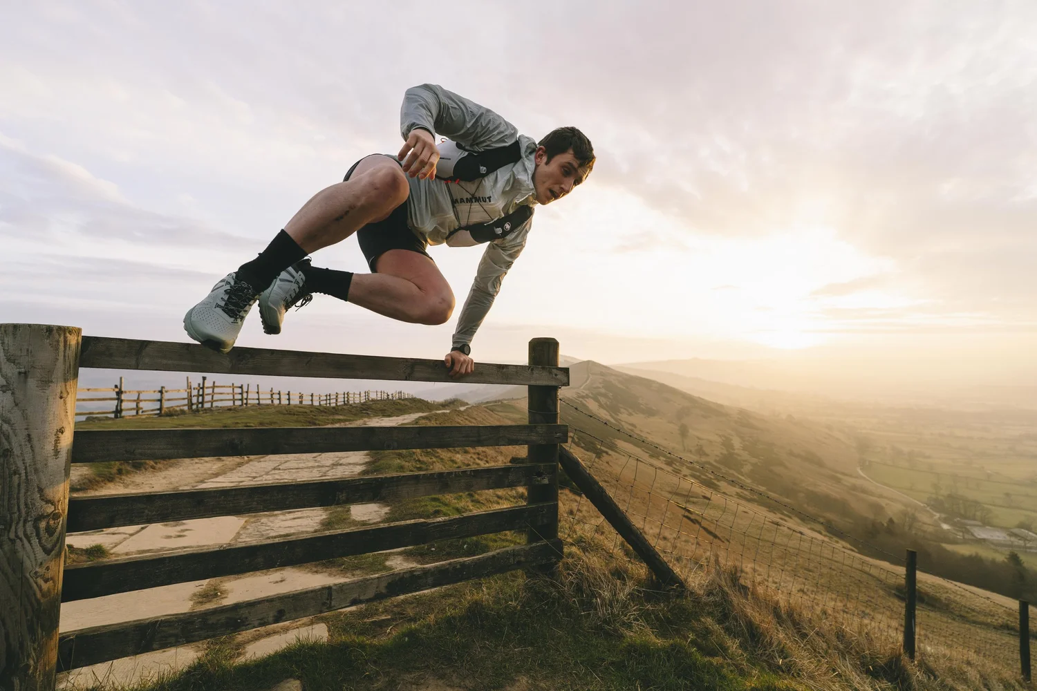 Trail runner leaping fence at sunset on Mam Tor